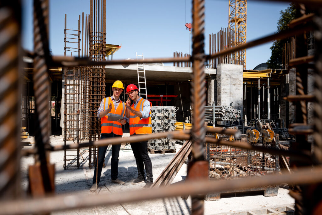 architect and structural engineer in orange work vests and helmets discuss a building project on the open air building site with a lot of steel frames